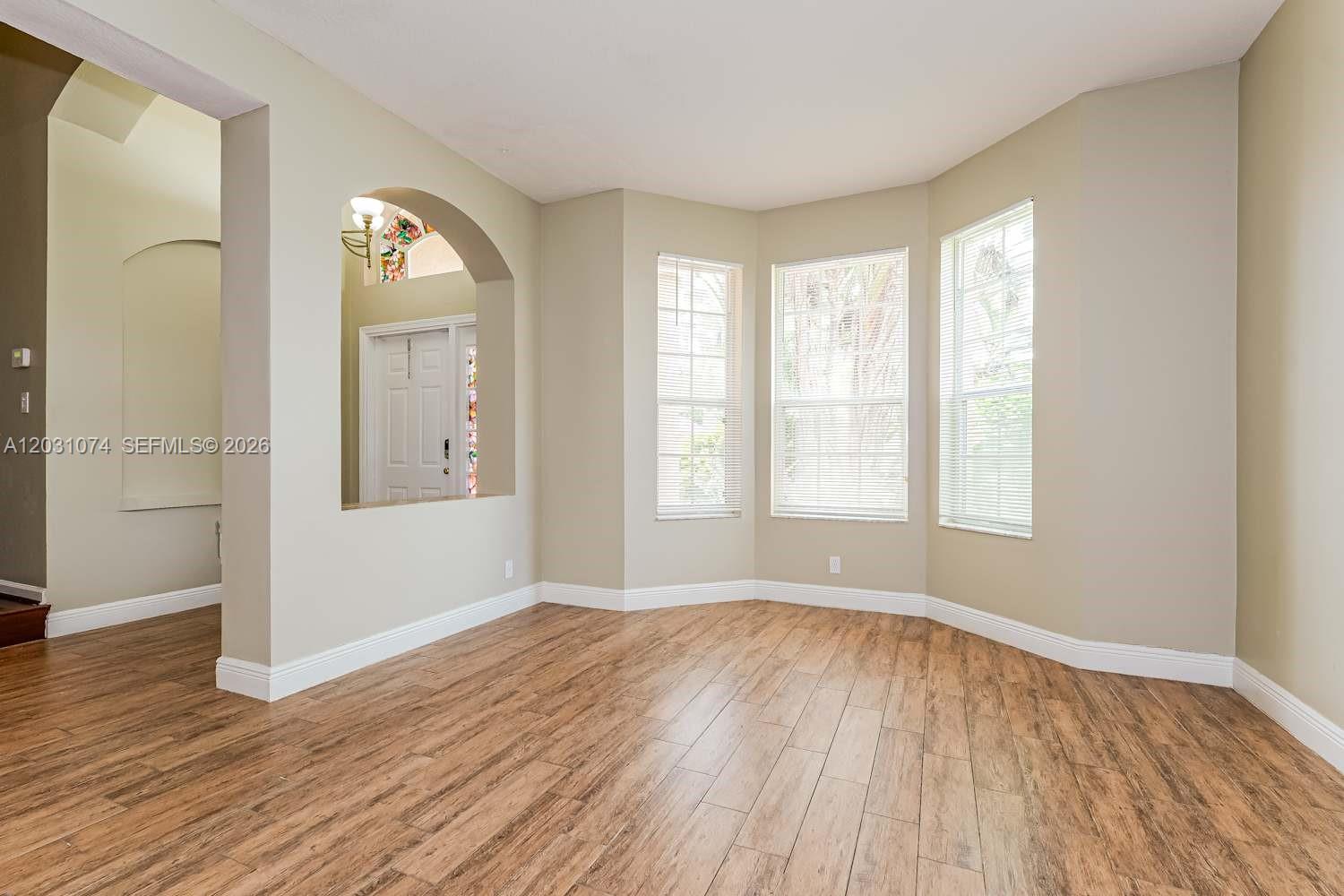 A room with light-colored walls, wood-look flooring, and a bay window with three windows — WELLINGTON, FL