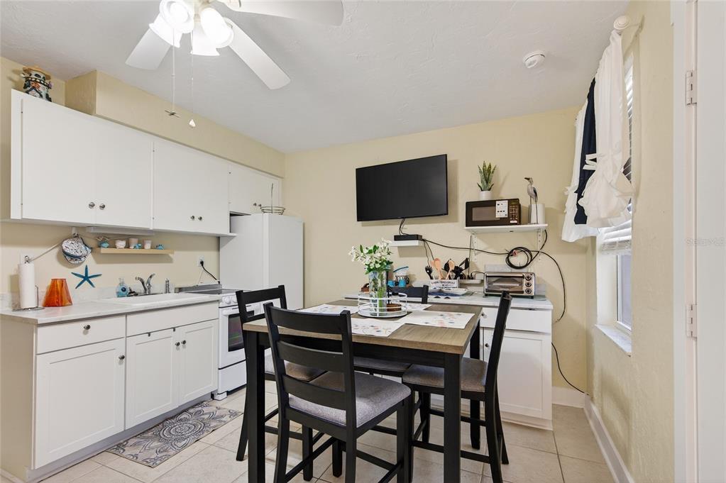 A small kitchen features white cabinets, a dining table, and a wall-mounted television — 908 VILLAS DRIVE UNIT 29, VENICE, FL