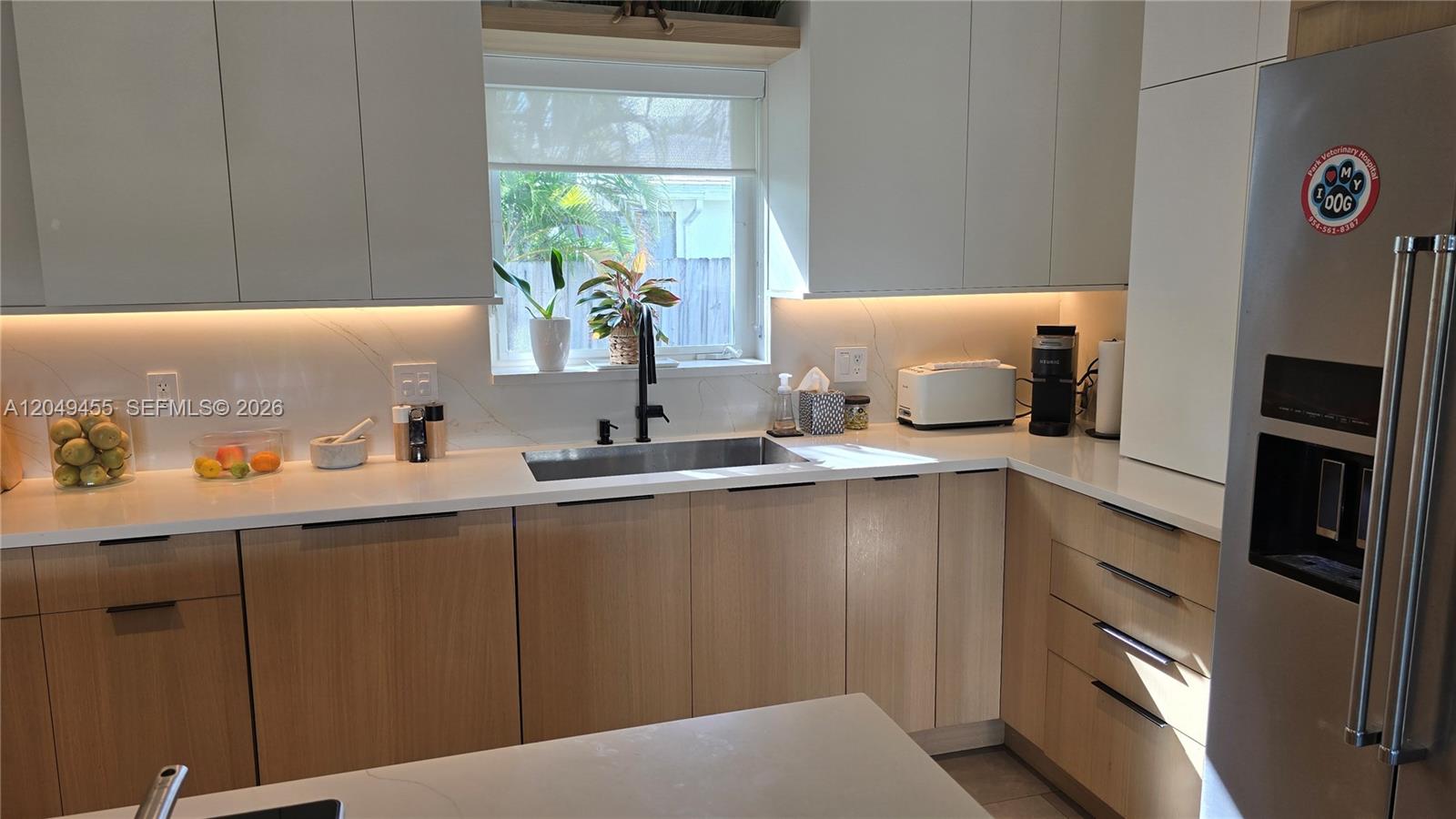 A modern kitchen features light wood lower cabinets, white upper cabinets, and white countertops — 800 Polk St, Hollywood FL 33019, HOLLYWOOD, FL