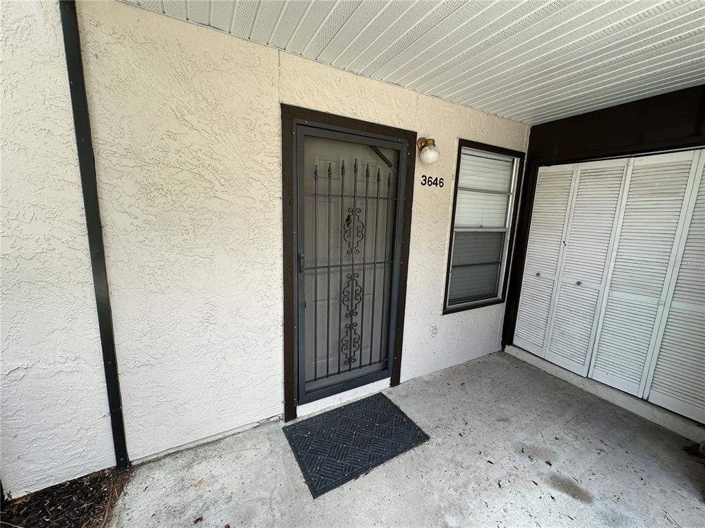 A concrete entryway features a security screen door, a window, and white louvered closet doors — 3646 59TH AVENUE W UNIT 3646, BRADENTON, FL