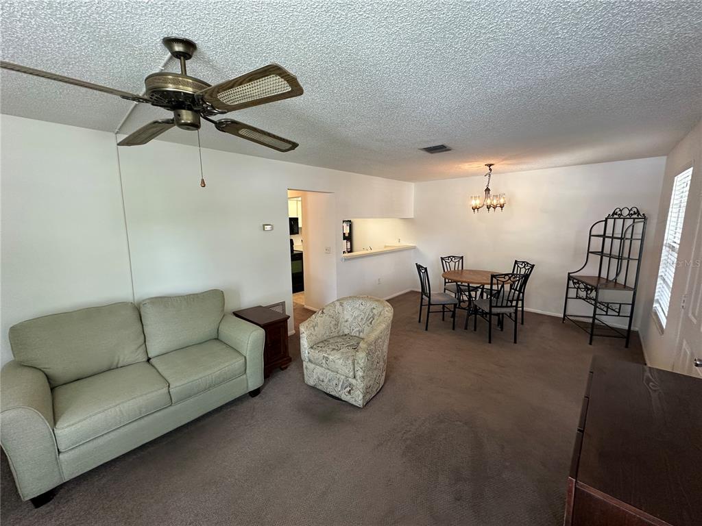 A living and dining room with brown carpet, a ceiling fan, and a dining set — 3646 59TH AVENUE W UNIT 3646, BRADENTON, FL