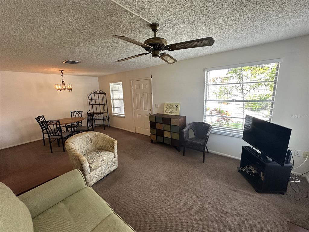 A living and dining area features carpeted flooring, a ceiling fan, and a large window — 3646 59TH AVENUE W UNIT 3646, BRADENTON, FL