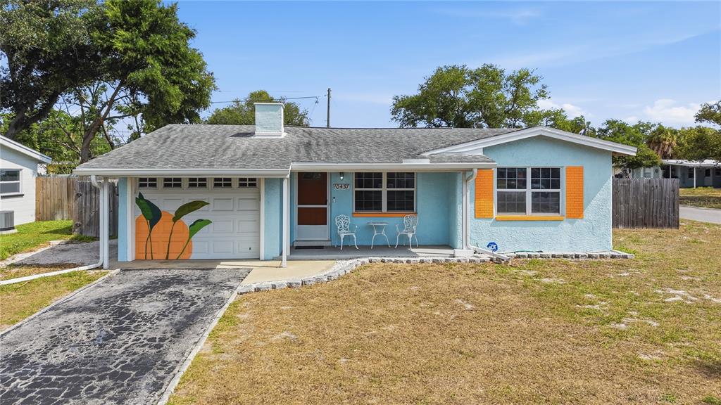 A light blue single-story house features an orange-painted garage door mural and orange window shutters — 10437 52ND AVENUE N, ST PETERSBURG, FL