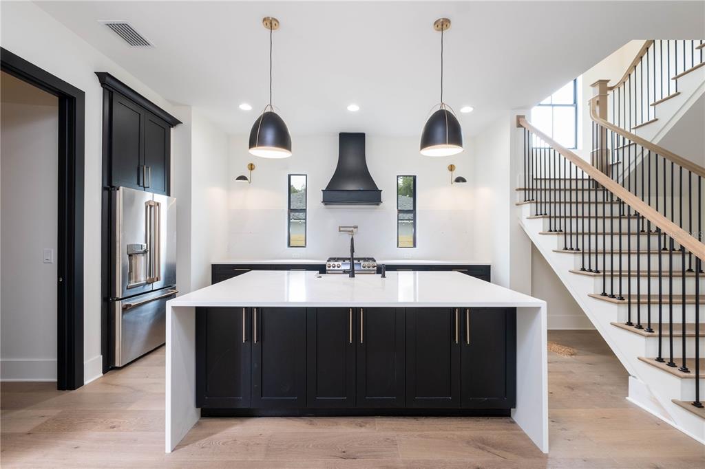 A modern kitchen features a large white island, black cabinetry, stainless steel appliances, and a staircase — 818 W KENTUCKY AVENUE, TAMPA, FL