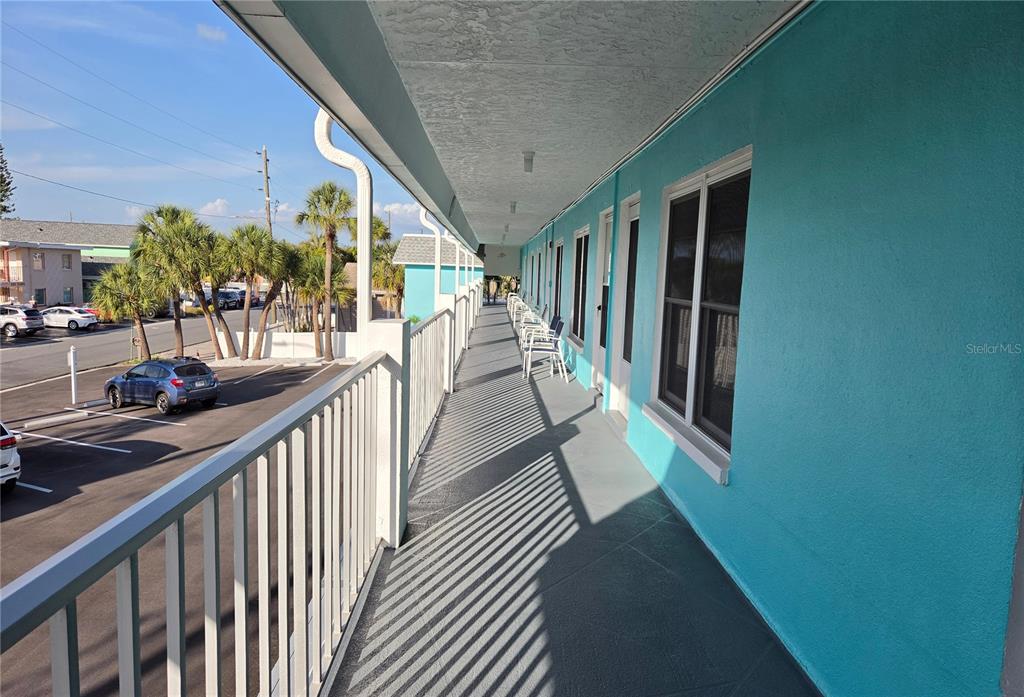 An outdoor balcony with a white railing overlooks a parking lot next to turquoise buildings — 680 71ST AVENUE UNIT 12, ST PETE BEACH, FL