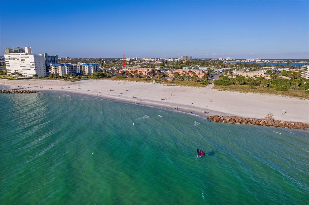 An aerial view of a sandy beach with turquoise water, coastal buildings, and a red arrow — 680 71ST AVENUE UNIT 12, ST PETE BEACH, FL