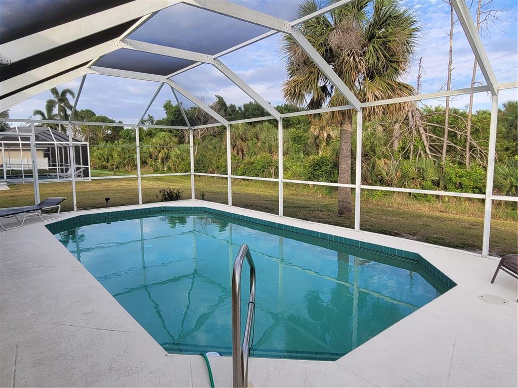 A swimming pool enclosed by a screened lanai overlooks a wooded backyard — 72 LONG MEADOW COURT, ROTONDA WEST, FL