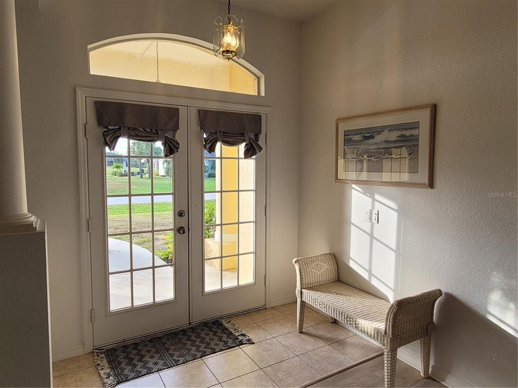 An entryway features a double glass door, tile flooring, a wicker bench, and a pendant light — 72 LONG MEADOW COURT, ROTONDA WEST, FL