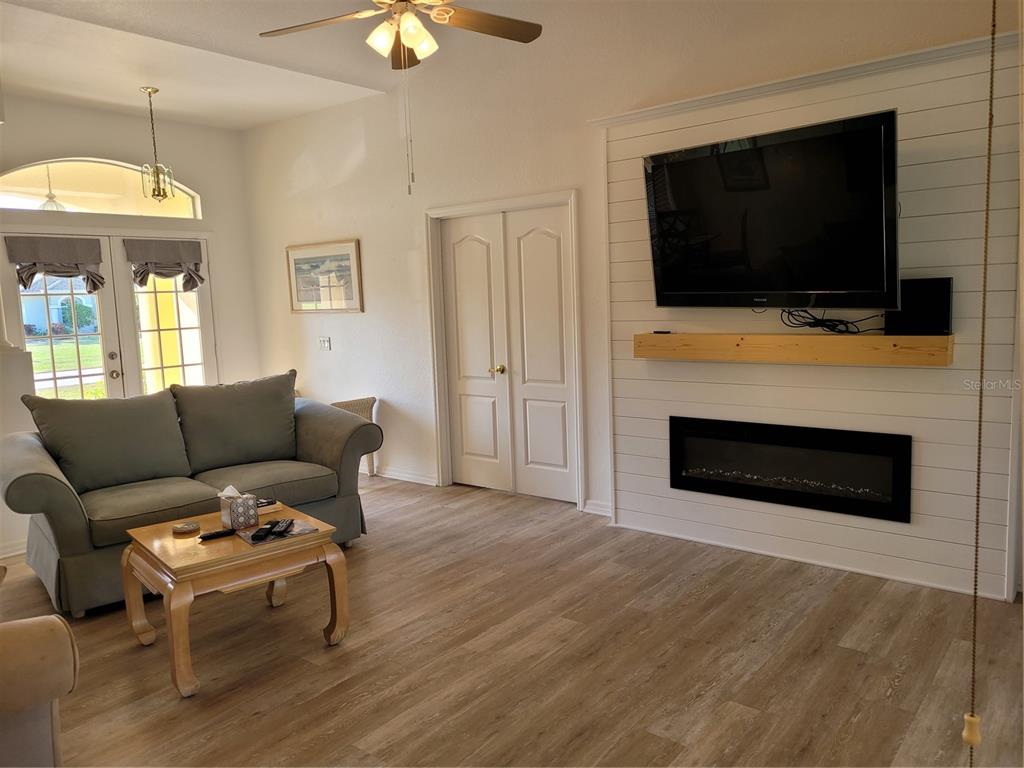 A living room features a shiplap fireplace wall, a gray sofa, and wood-look flooring — 72 LONG MEADOW COURT, ROTONDA WEST, FL