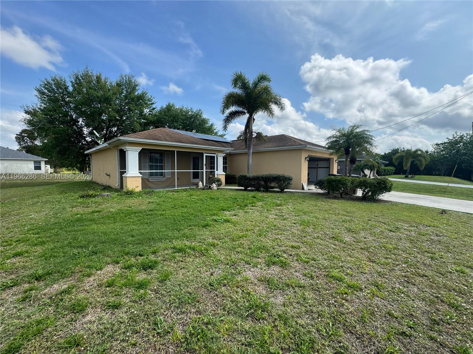 A single-story tan house features a screened-in front porch, a garage, and palm trees — 507 Peerless Cir, Lehigh Acres FL 33974, LEHIGH ACRES, FL