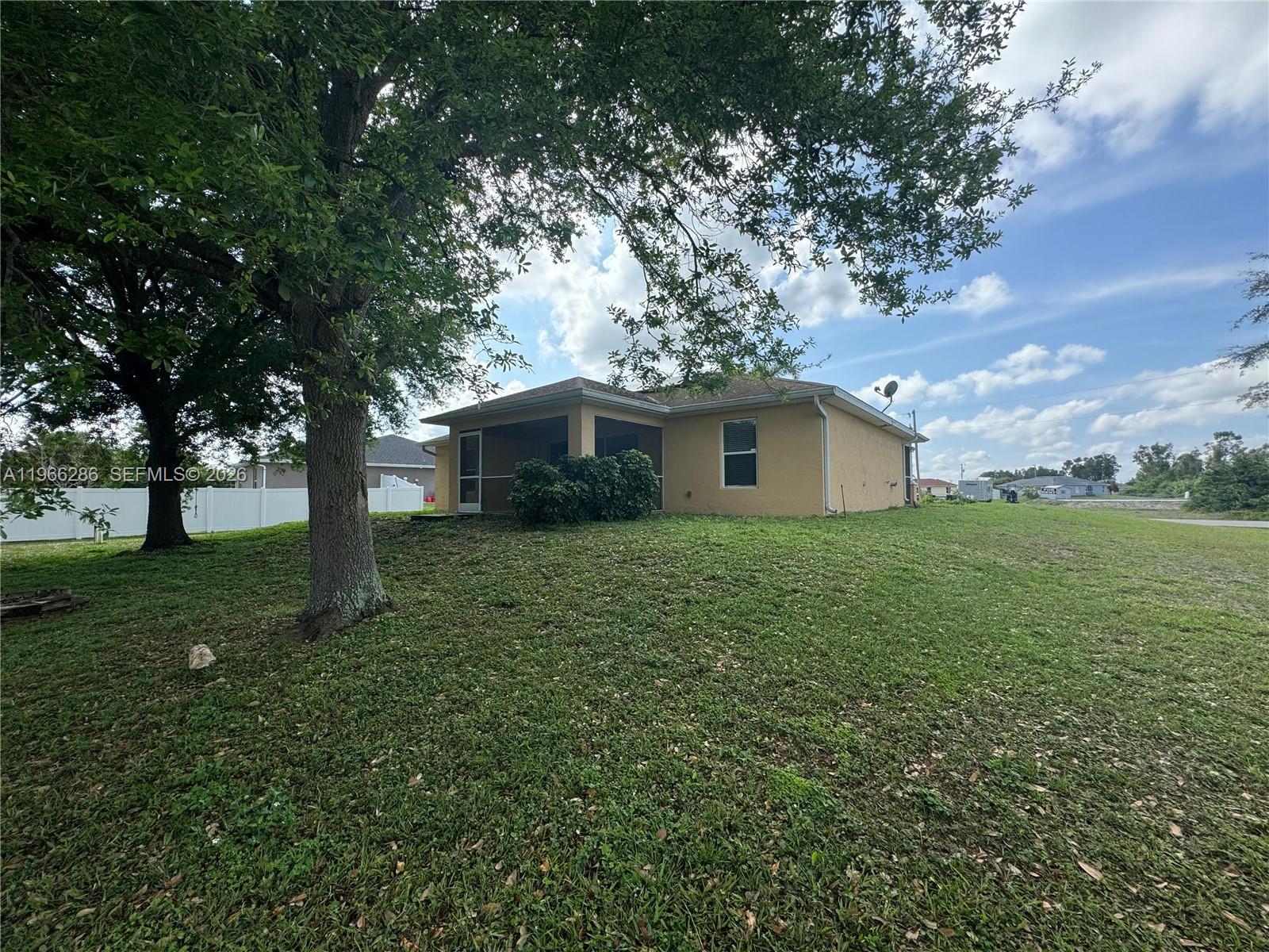 A tan house with a screened-in porch sits on a large, grassy lot with trees — 507 Peerless Cir, Lehigh Acres FL 33974, LEHIGH ACRES, FL