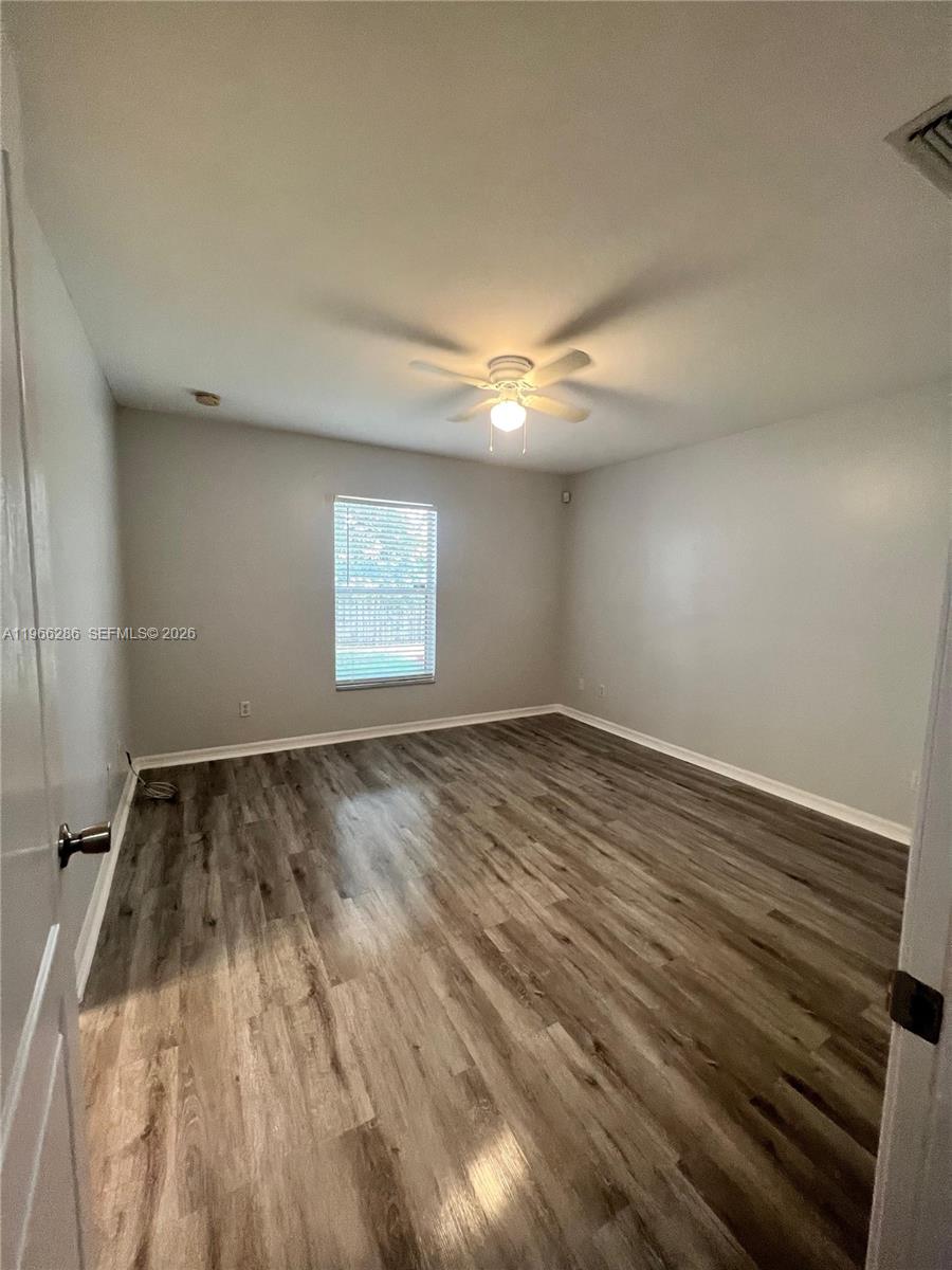An empty bedroom features light gray walls, a ceiling fan, and wood-look laminate flooring — 507 Peerless Cir, Lehigh Acres FL 33974, LEHIGH ACRES, FL