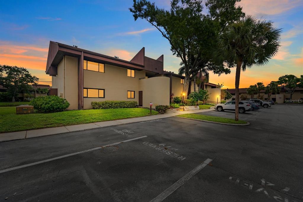 A multi-story apartment building exterior with a parking lot in the foreground at sunset — 875 S VILLAGE DRIVE N UNIT 101, ST PETERSBURG, FL