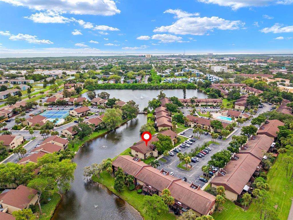 An aerial view shows a residential complex with brown-roofed buildings surrounding a central lake — 875 S VILLAGE DRIVE N UNIT 101, ST PETERSBURG, FL