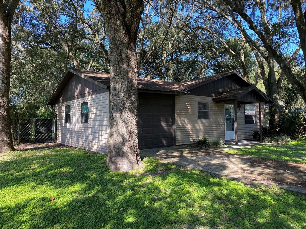 A single-story house with beige siding, a dark brown garage door, and surrounding mature trees — 39648 MEADOWOOD LOOP, ZEPHYRHILLS, FL