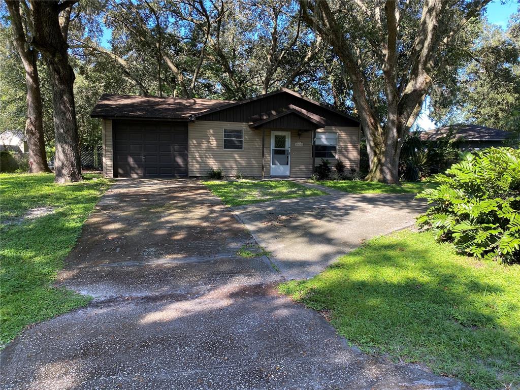 A single-story house with a garage, tan siding, and a concrete driveway under large trees — 39648 MEADOWOOD LOOP, ZEPHYRHILLS, FL