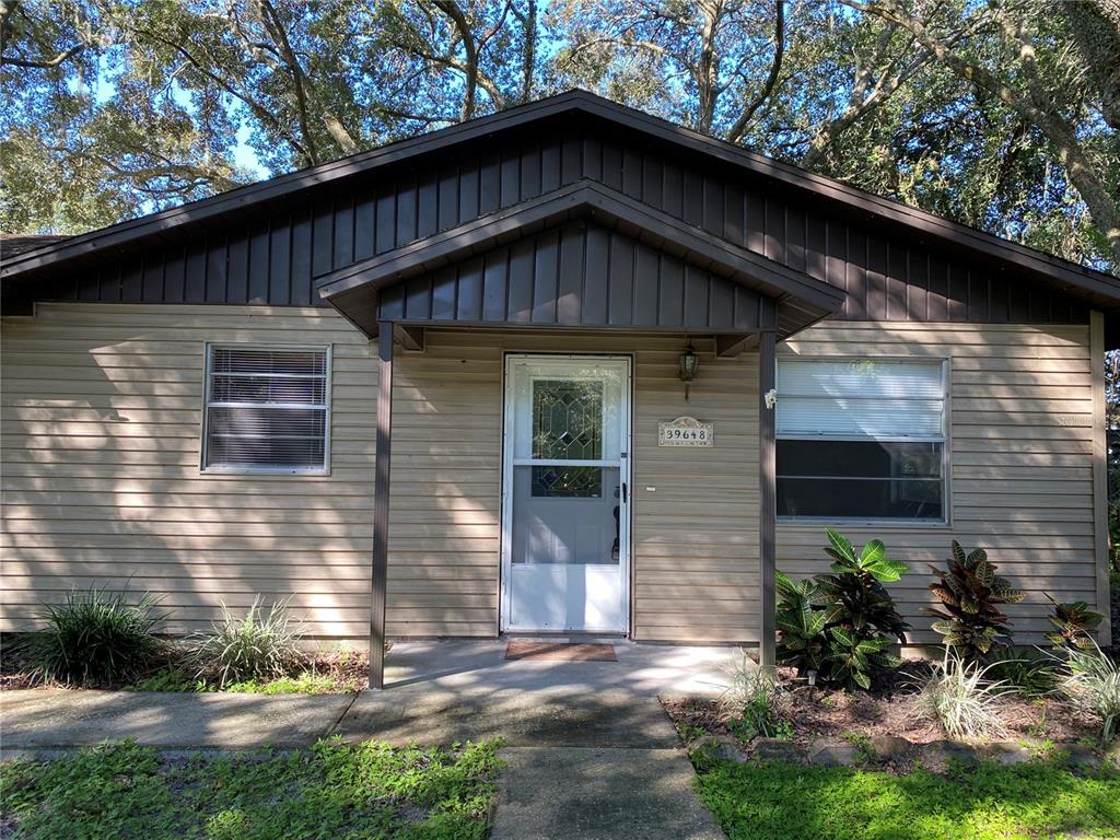 A single-story house with tan horizontal siding, a dark brown gable roof, and a front porch — 39648 MEADOWOOD LOOP, ZEPHYRHILLS, FL