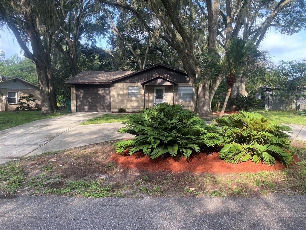 A single-story house with a garage, tan siding, and large trees in the front yard — 39648 MEADOWOOD LOOP, ZEPHYRHILLS, FL