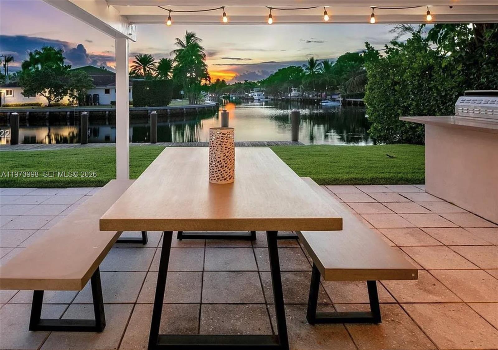 An outdoor patio features a wooden dining table with benches overlooking a canal at sunset — 524 Oleander Dr, Hallandale Beach FL 33009, HALLANDALE BEACH, FL