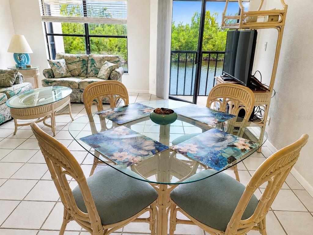 A dining area with a glass table and wicker chairs overlooks a water view — 3256 WHITE IBIS COURT UNIT 325, PUNTA GORDA, FL