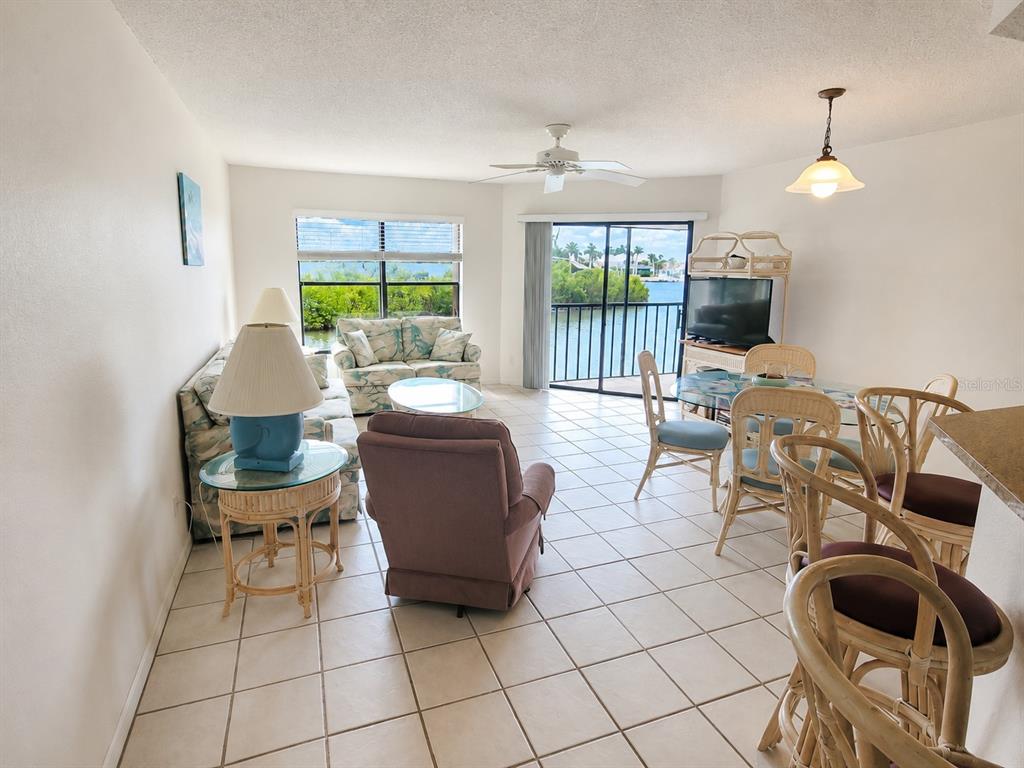 A living and dining area with tile floors, wicker furniture, and a balcony overlooking water — 3256 WHITE IBIS COURT UNIT 325, PUNTA GORDA, FL