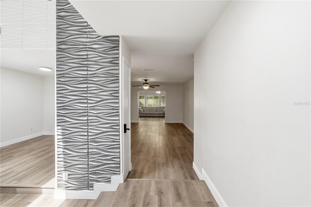 A hallway with wood-look flooring leads to a living area featuring a textured silver wall — 758 N GRETNA COURT, WINTER SPRINGS, FL