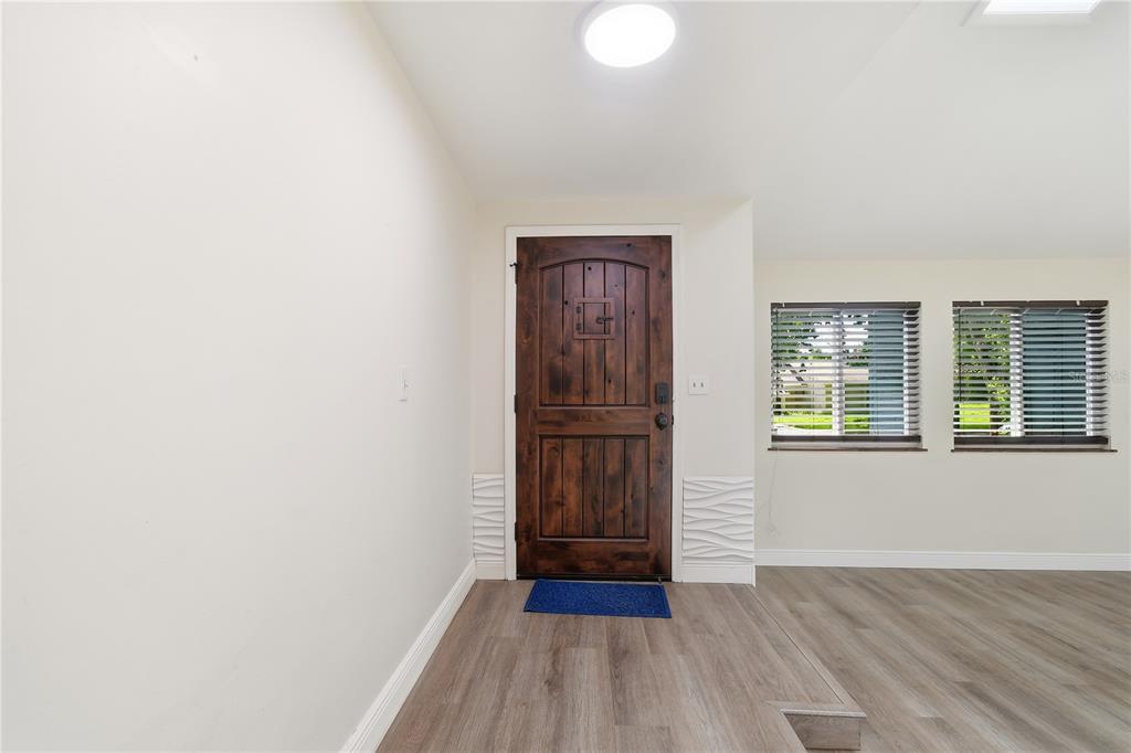 An entryway features a dark wood front door, light-colored walls, and gray wood-look flooring — 758 N GRETNA COURT, WINTER SPRINGS, FL