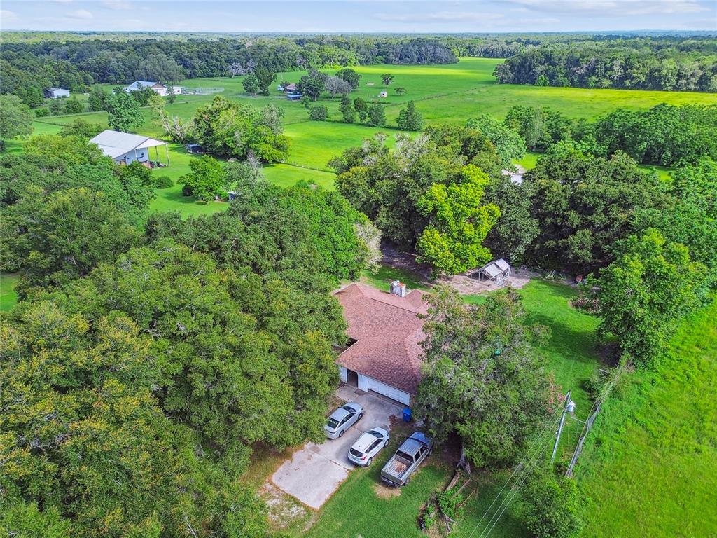An aerial view shows a house with a brown roof, three parked cars, and surrounding trees — 18139 BENES ROUSH ROAD, BROOKSVILLE, FL