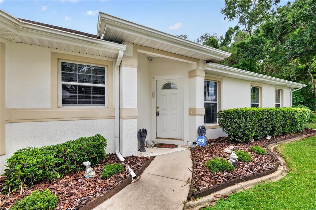A single-story house exterior features a white door, tan trim, and a landscaped front yard — 27545 DISCOVER COURT, LEESBURG, FL