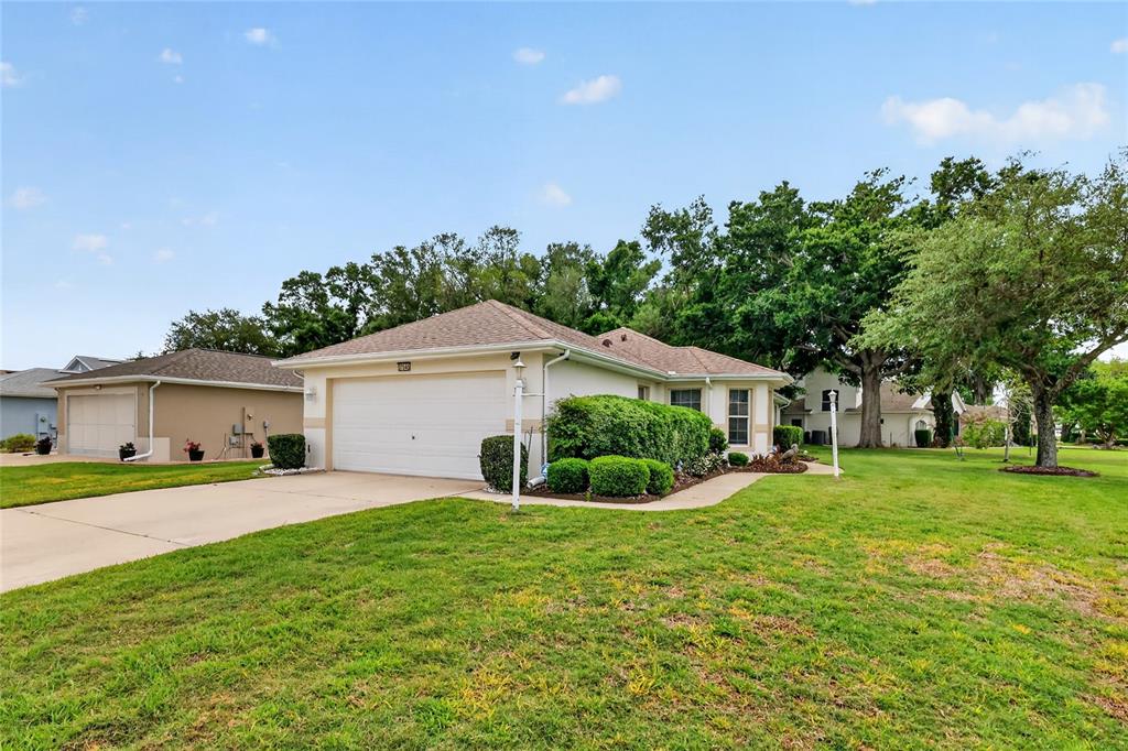 A single-story house with a white garage door, beige siding, and a landscaped front yard — 27545 DISCOVER COURT, LEESBURG, FL
