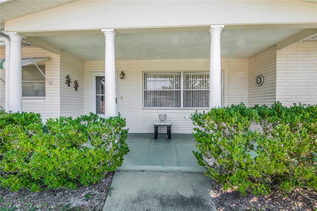 A covered front porch features white brick walls, three columns, and two large green bushes — 91 S LEE STREET, BEVERLY HILLS, FL