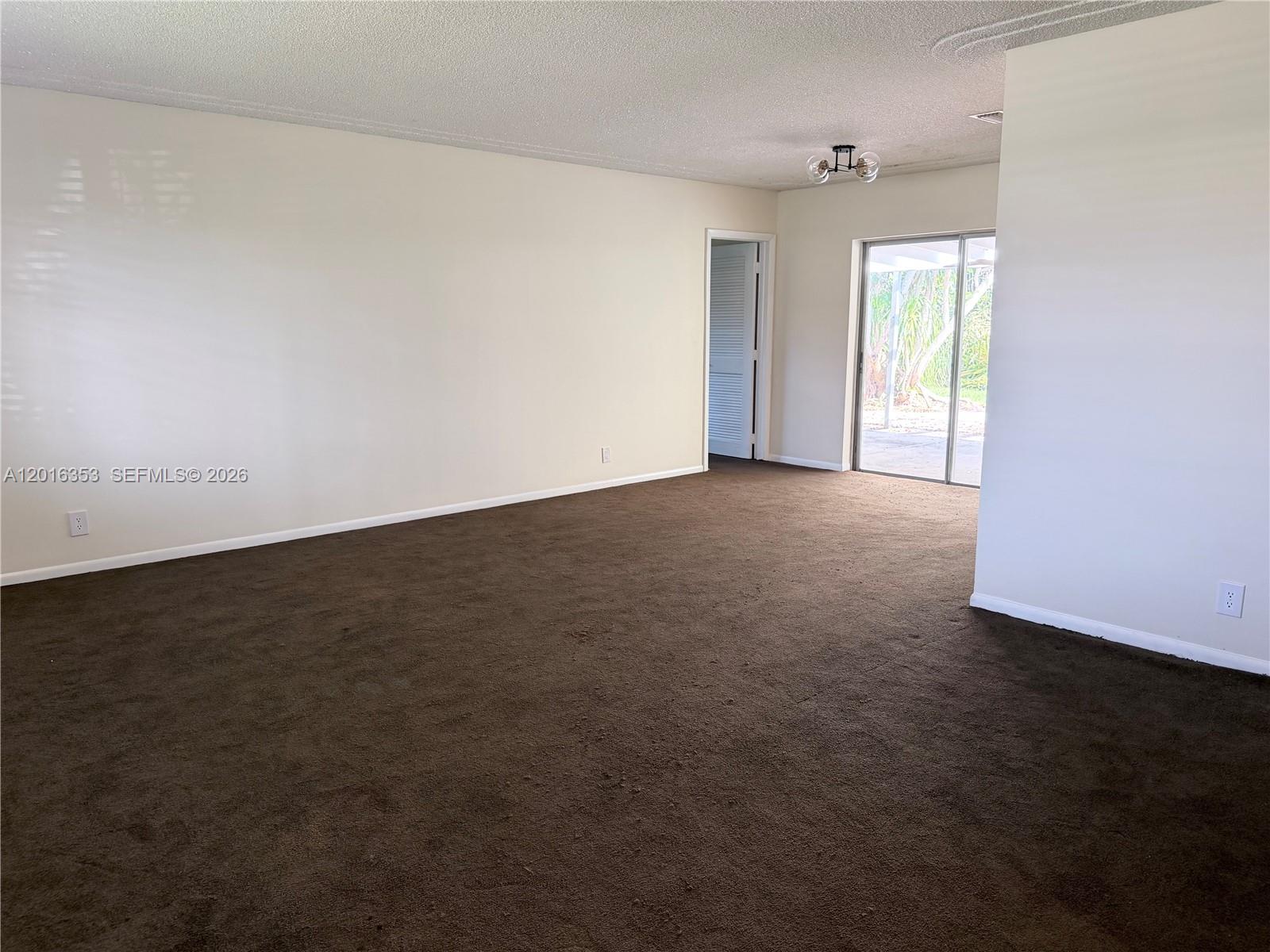 An empty room features brown carpeting, off-white walls, a ceiling light, and a sliding glass door — 4420 NW 16th St, Lauderhill FL 33313, LAUDERHILL, FL