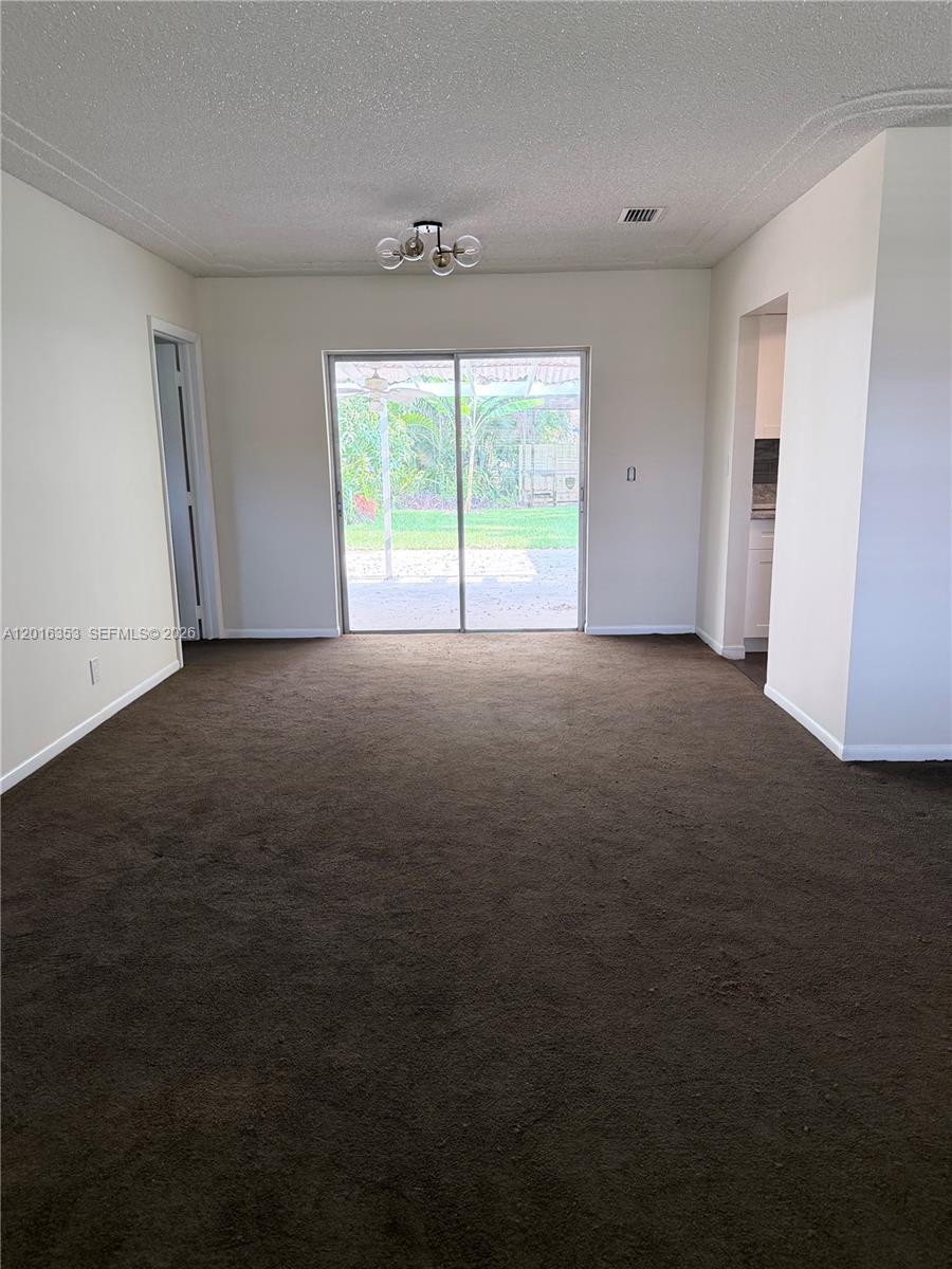 An empty room with dark brown carpeting, a sliding glass door, and a ceiling light — 4420 NW 16th St, Lauderhill FL 33313, LAUDERHILL, FL