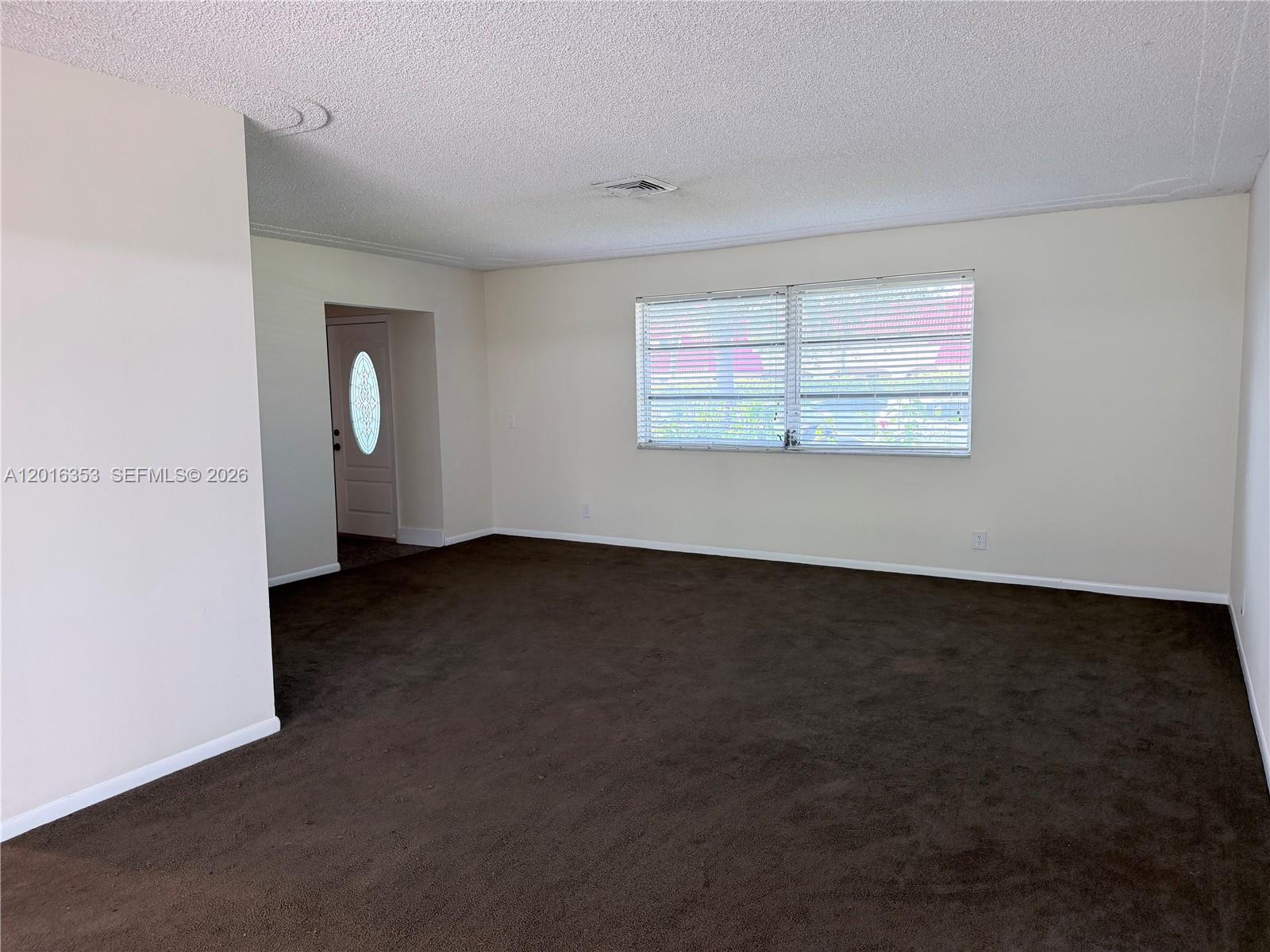 An empty room features dark brown carpeting, off-white walls, and a window with blinds — 4420 NW 16th St, Lauderhill FL 33313, LAUDERHILL, FL