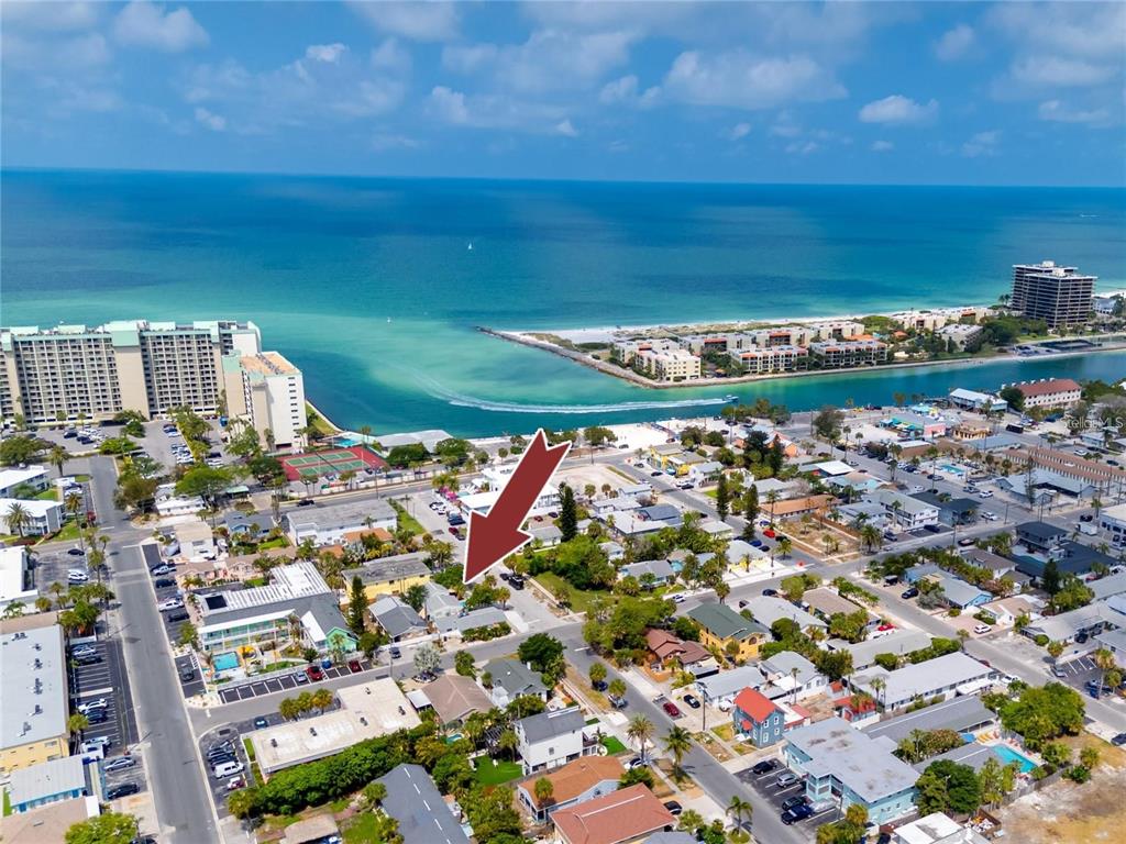 An aerial view shows a coastal neighborhood with a red arrow pointing to a house — 610 72ND AVENUE, ST PETE BEACH, FL