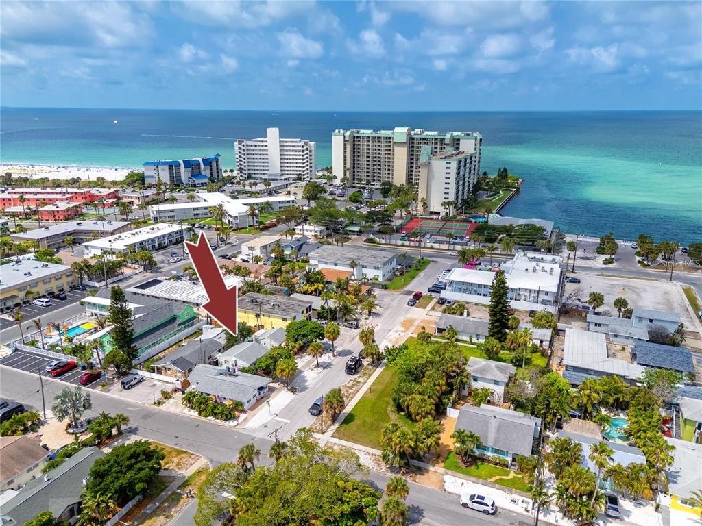 An aerial view shows a coastal neighborhood with a red arrow pointing to a house — 610 72ND AVENUE, ST PETE BEACH, FL