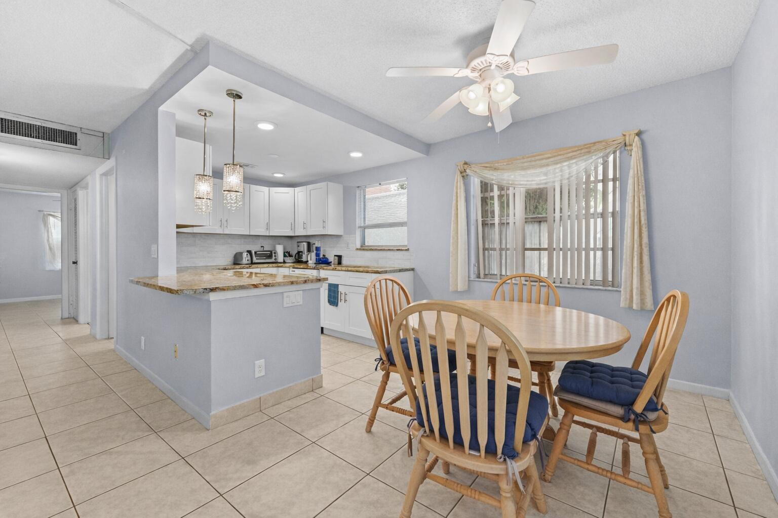A kitchen with white cabinets and granite countertops opens to a dining area with chairs — 211 Piedmont E, Delray Beach FL 33484, DELRAY BEACH, FL