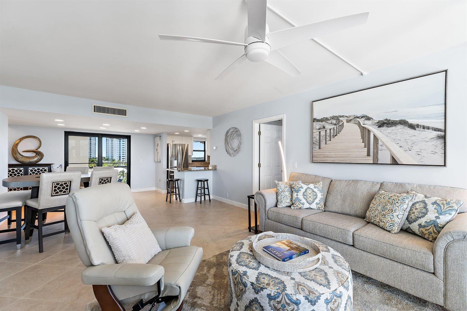 A living room with a beige sofa, patterned ottoman, white armchair, and an open kitchen — 336 Golfview Road # 619, North Palm Beach FL 33408, NORTH PALM BEACH, FL