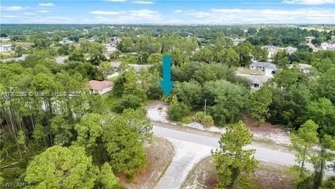 An aerial view shows a vacant, wooded residential lot marked by a blue arrow — 2514 38TH ST, Lehigh Acres FL 33971, LEHIGH ACRES, FL