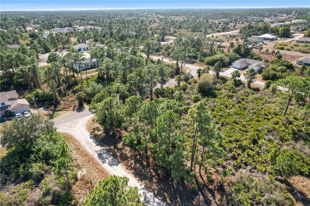 An aerial view shows a vacant, wooded residential lot situated between paved roads and houses — 774 KIRKMAN AVENUE, LEHIGH ACRES, FL