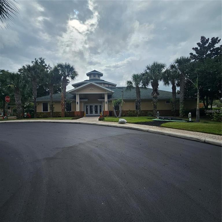 A single-story community clubhouse with a cupola, palm trees, and a paved circular driveway — 9055 TREASURE TROVE LANE UNIT 201, KISSIMMEE, FL