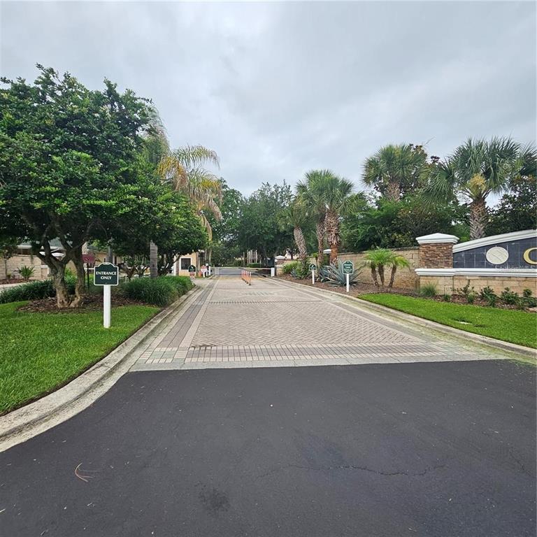 A paved driveway leads to the gated entrance of a residential community with palm trees — 9055 TREASURE TROVE LANE UNIT 201, KISSIMMEE, FL