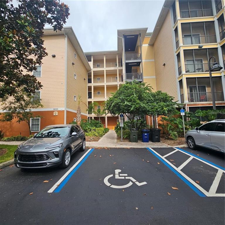 A multi-story apartment building exterior features a paved parking lot with a designated accessible space — 9055 TREASURE TROVE LANE UNIT 201, KISSIMMEE, FL