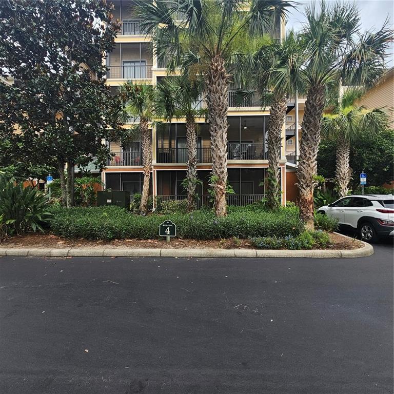 A multi-story apartment building with screened balconies stands behind palm trees and landscaping — 9055 TREASURE TROVE LANE UNIT 201, KISSIMMEE, FL