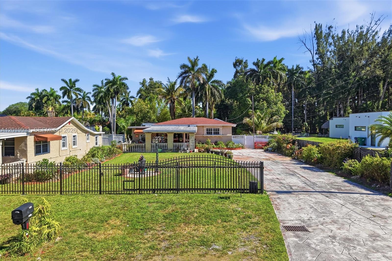 A single-story house with a fenced front yard and a paved driveway under a blue sky — 55-57 NE 156th St, Miami FL 33162, MIAMI, FL