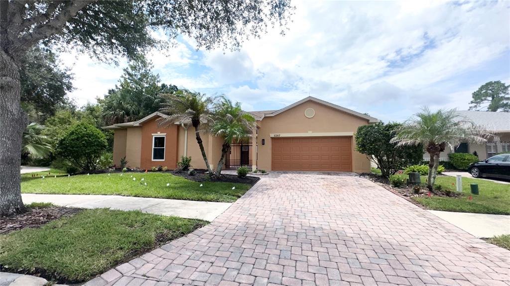 A single-story house with a tan exterior, a two-car garage, and a brick paver driveway — 1287 GLENDORA ROAD, POINCIANA, FL