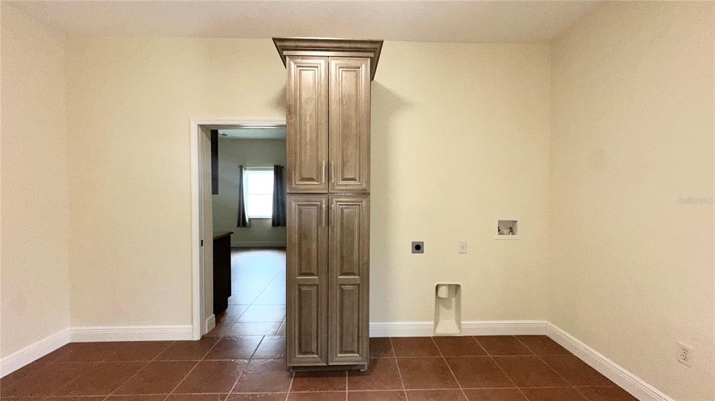 A laundry room features a tall wooden storage cabinet, tiled flooring, and utility hookups — 1287 GLENDORA ROAD, POINCIANA, FL