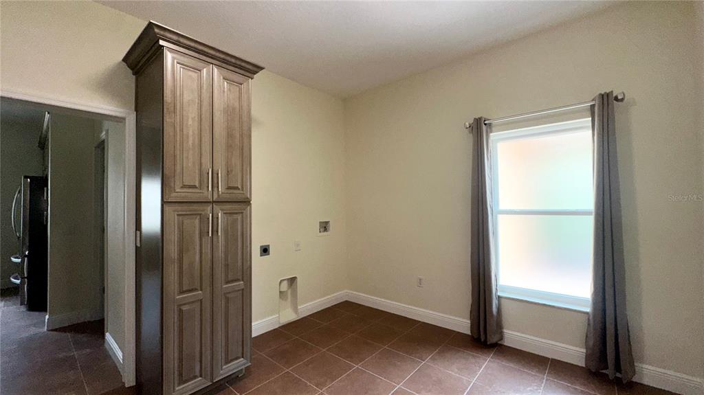 A laundry room features tile flooring, a tall wooden storage cabinet, and a window with curtains — 1287 GLENDORA ROAD, POINCIANA, FL