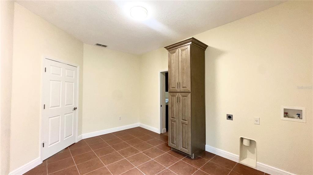A laundry room features tile flooring, a tall wooden cabinet, and wall-mounted utility connections — 1287 GLENDORA ROAD, POINCIANA, FL
