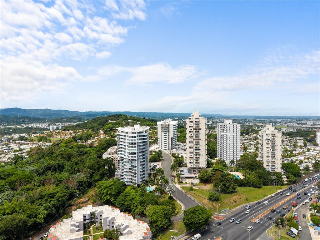 An aerial view shows several high-rise apartment buildings surrounded by lush greenery and a highway — 14 CARR 833 UNIT 1404, GUAYNABO, PR